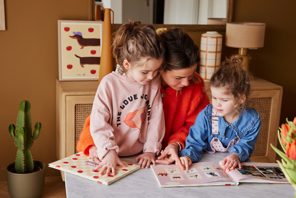 Une maman lit des imagiers personnalisés à ses deux petites filles assisent à une table